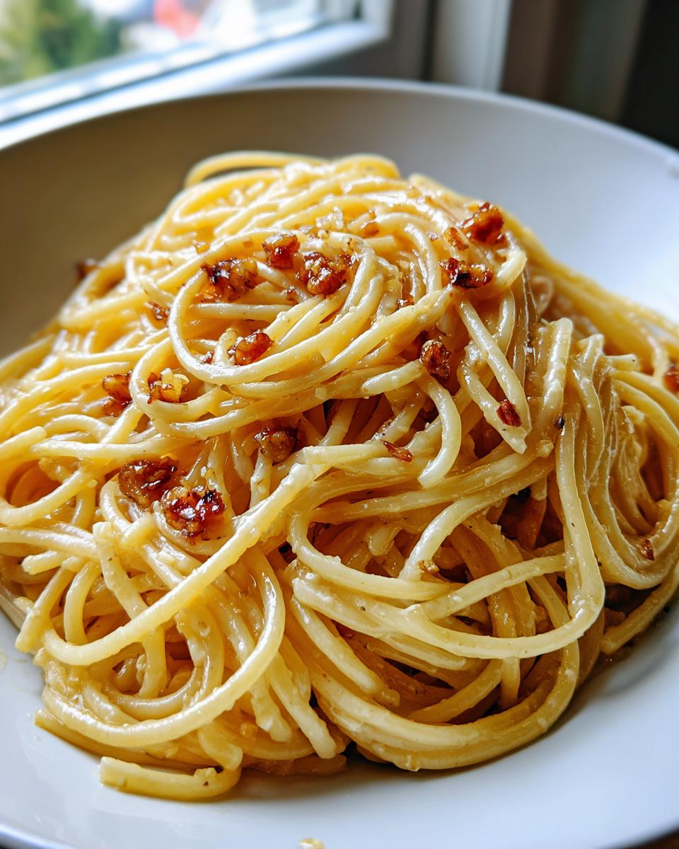 A close-up shot of perfectly coated, creamy garlic noodles topped with browned bits of garlic or crispy shallots.