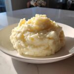 A generous serving of fluffy, creamy mashed potatoes piled high on a white plate.