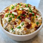 A close-up of the rich Neiman Marcus Dip served in a white bowl, generously topped with bacon bits, shredded cheese, sliced almonds, and green onions.