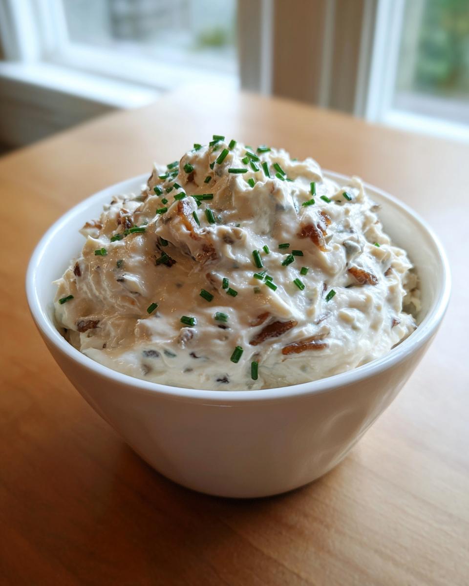 A white bowl filled with creamy onion dip, garnished generously with chopped green chives.