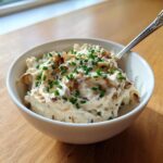 A white bowl filled with creamy onion dip, garnished generously with fresh chives and crispy fried onions.