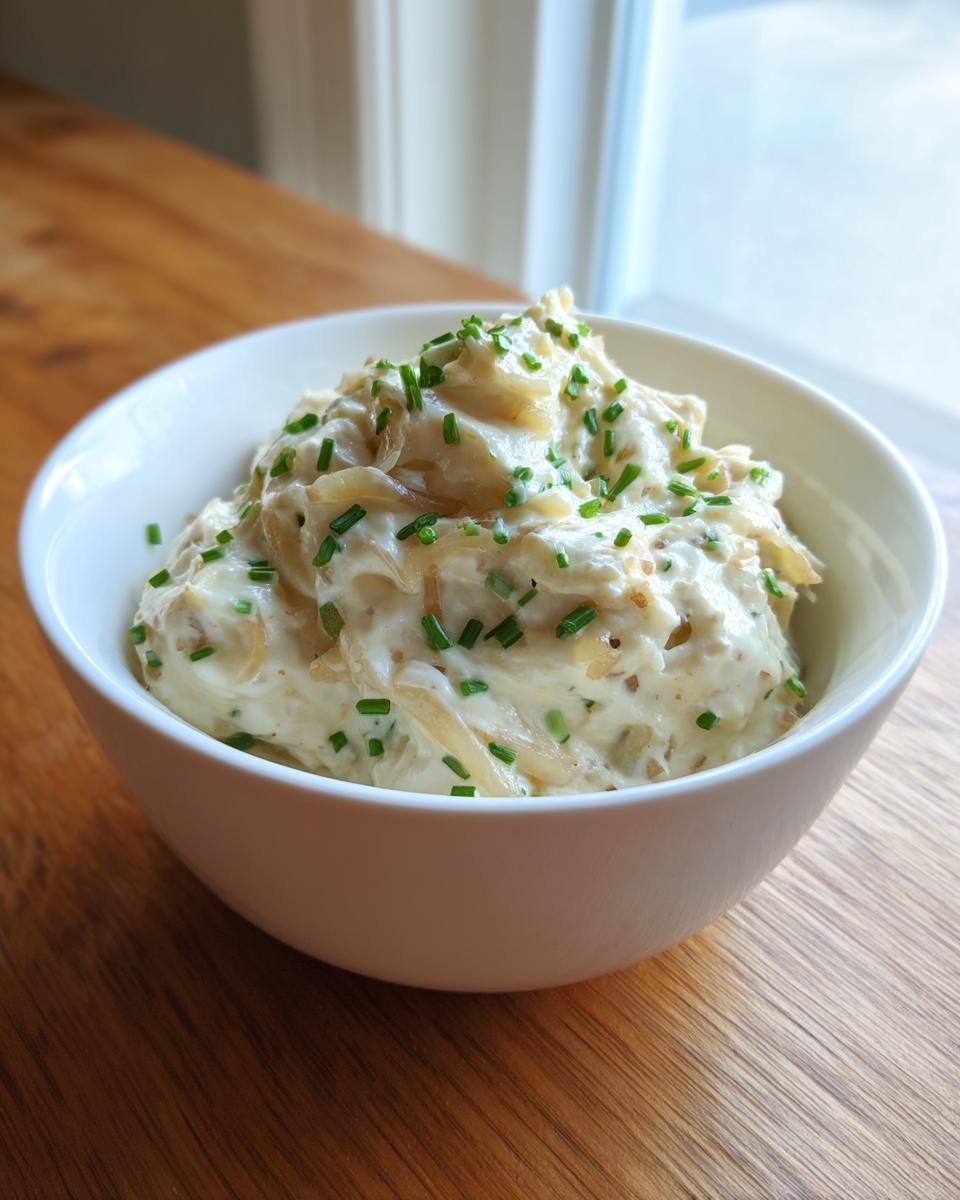 A white bowl filled with rich, creamy onion dip featuring caramelized onions and topped with fresh green chives.