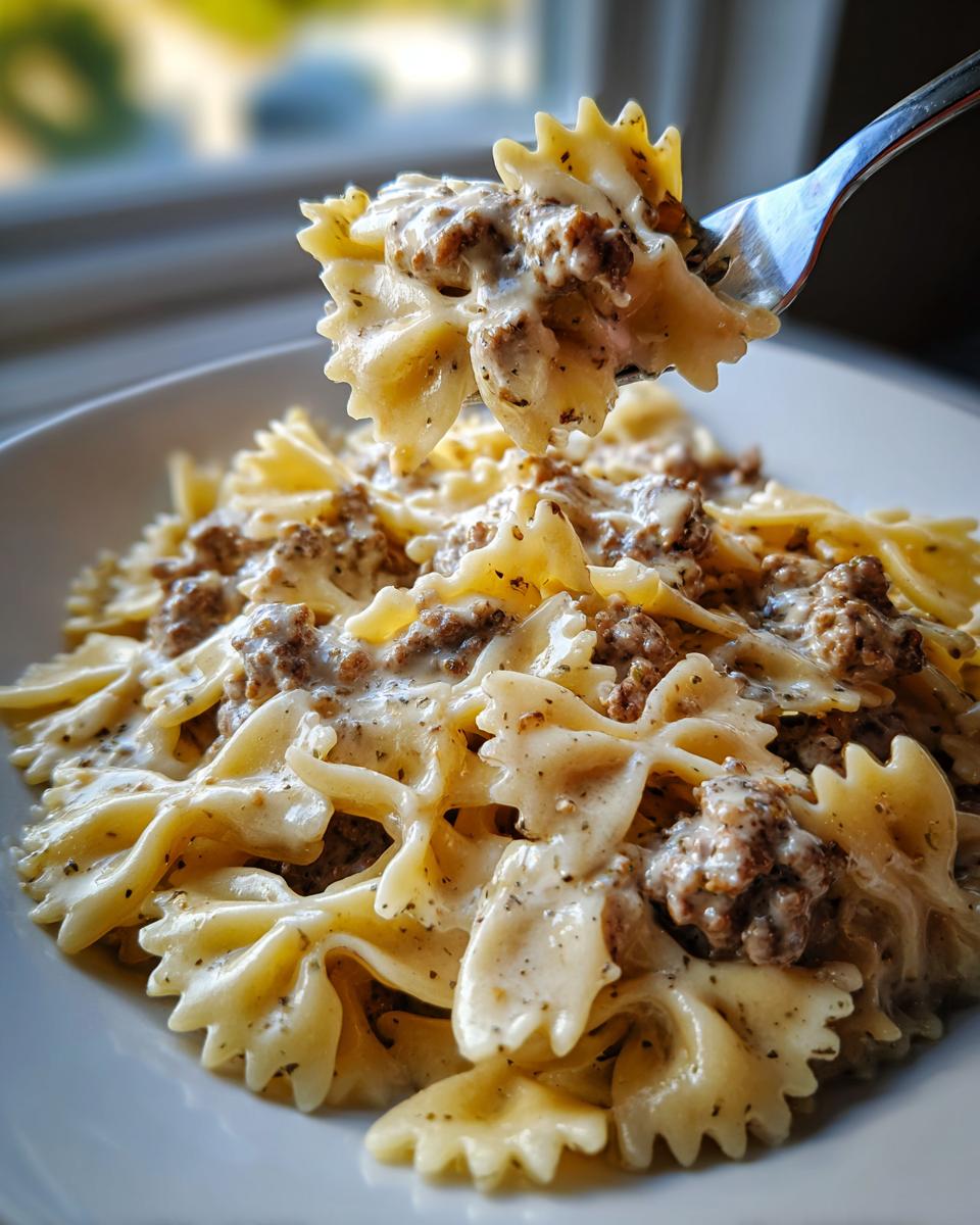 A fork lifting a bite of creamy parmesan garlic beef bowtie pasta from a white bowl.