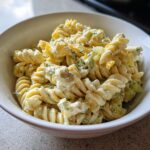 Close-up of creamy pickle pasta salad made with rotini pasta, visible chunks of pickle, and herbs in a white bowl.