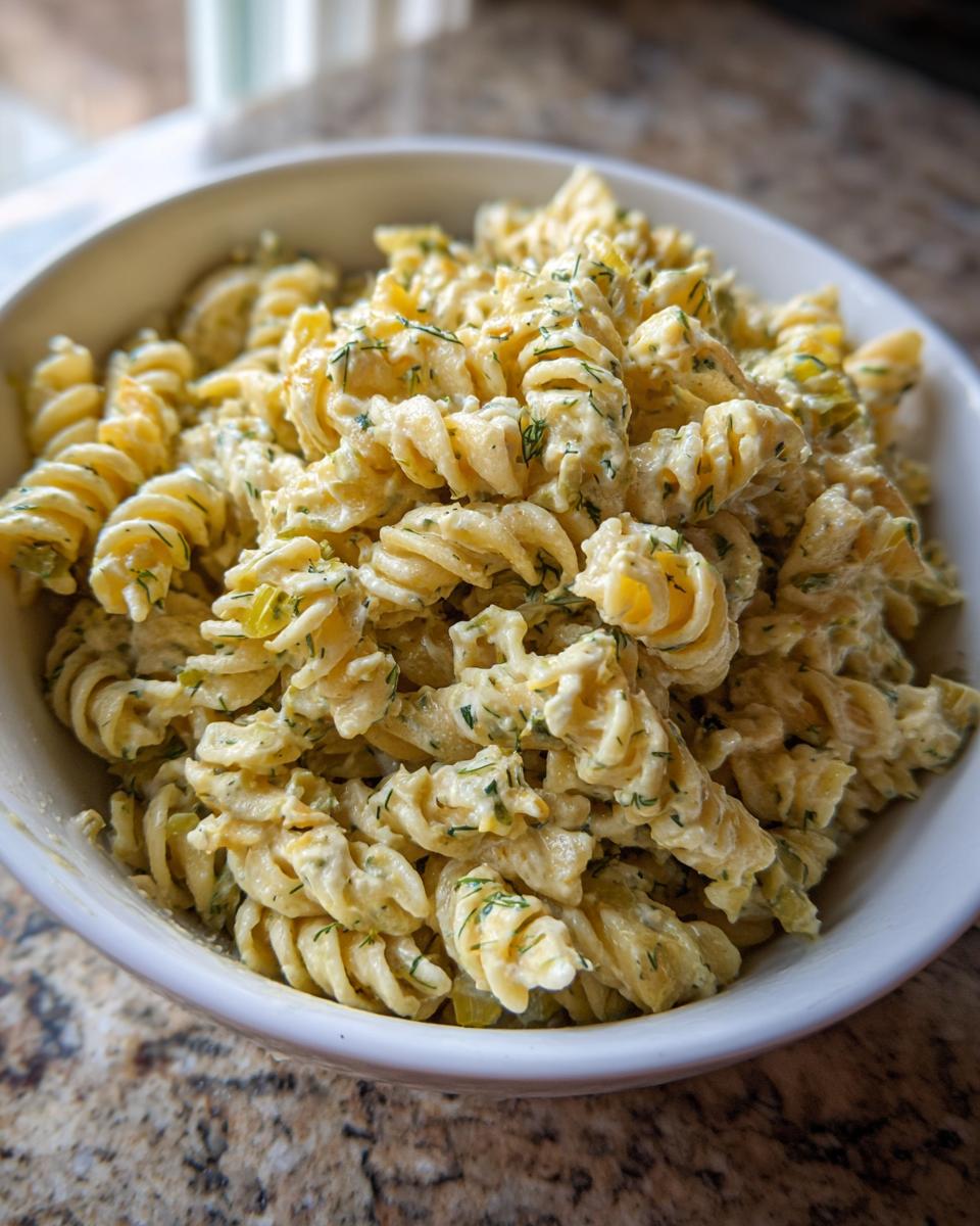 Close-up of creamy pickle pasta salad made with fusilli pasta and fresh dill in a white bowl.
