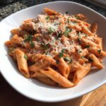 A white bowl filled with penne pink sauce pasta, topped generously with grated Parmesan cheese and fresh parsley.