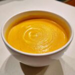Close-up of a white bowl filled with vibrant orange pumpkin soup, swirled with cream.