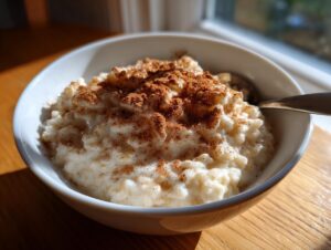 A close-up of creamy rice pudding served in a white bowl, generously dusted with cinnamon.