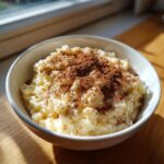 A close-up of creamy rice pudding served in a white bowl, generously dusted with cinnamon.
