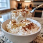 A spoonful of creamy rice pudding recipe topped with cinnamon being lifted from a white bowl.