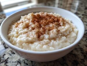 A close-up of a white bowl filled with creamy rice pudding recipe topped generously with ground cinnamon.