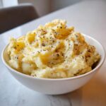 A white bowl filled with creamy slow cooker mashed potatoes topped generously with melted butter and cracked black pepper.
