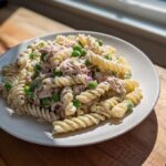 A plate of creamy tuna pasta salad made with rotini pasta, tuna, green peas, and red onion, served on a white plate.