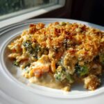 A serving of creamy vegetable casserole featuring broccoli and carrots, topped with a crunchy, golden brown breadcrumb crust.