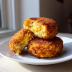 Three golden-brown, crispy potato croquettes stacked on a white plate, one cut open showing the soft interior.