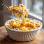 A spoonful of creamy crockpot cheesy potatoes being lifted, showing extreme cheese pull.