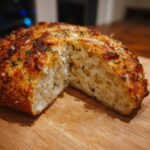 A round loaf of crusty garlic cheese bread, cut in half to show the soft interior crumb.