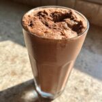 Close-up of a tall glass filled with thick, blended frozen hot chocolate, topped with cocoa powder.