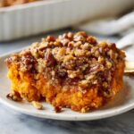 A close-up shot of a serving of easy sweet potato casserole topped with a crunchy pecan and brown sugar crumble.