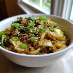 Close-up of a white bowl filled with savory egg roll in a bowl mixture, topped with green onions and sesame seeds.