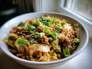 A close-up of a white bowl filled with savory egg roll in a bowl mixture, topped with green onions and sesame seeds.