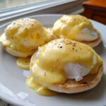 Three servings of Eggs Benedict topped generously with rich, creamy hollandaise sauce and cracked black pepper.