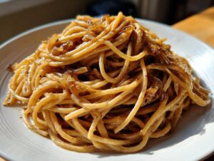 A close-up of a mound of spaghetti coated in a creamy sauce and topped with rich caramelized onion pasta.