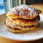 A tall stack of golden brown oatmeal pancakes dusted heavily with powdered sugar.