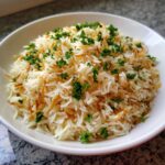 A bowl of fluffy rice pilaf mixed with toasted vermicelli noodles and topped with fresh chopped parsley.