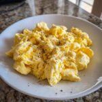 A close-up of creamy, fluffy scrambled eggs seasoned generously with black pepper on a white plate.