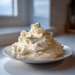 A large, fluffy mound of freshly made vanilla buttercream frosting sitting on a white plate.
