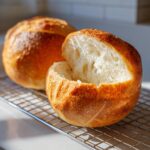 Close-up of one hollowed-out bread bowl ready for soup, with another loaf behind it on a cooling rack.