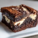 A rich, fudgy square of cream cheese brownies showing swirls of white cream cheese baked into the dark chocolate base.