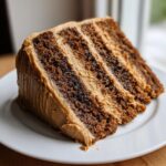 A tall slice of multi-layered gingerbread latte cake with rich brown cake layers and light brown coffee-colored frosting.