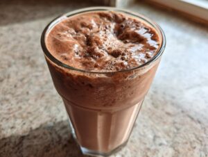 Close-up of a frothy, blended glass of frozen hot chocolate sitting on a speckled countertop.