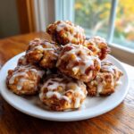 A stack of golden brown apple fritter bites drizzled with white vanilla glaze on a white plate.
