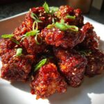 Close-up of glossy, dark red glazed korean fried chicken recipe pieces garnished with sesame seeds and green onions.