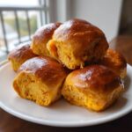 A close-up stack of freshly baked, glossy sweet potato rolls with a rich orange interior.