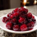 A close-up of a generous mound of glistening, deep red cherry pie filling served on a small white plate.
