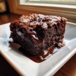 A rich, dark slice of chocolate pudding cake with warm, gooey sauce dripping down the side.
