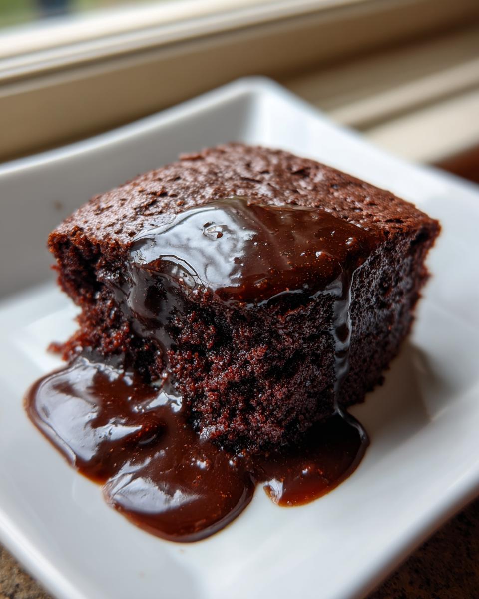 Close-up of a rich, dark chocolate pudding cake slice covered in warm, glossy chocolate sauce.