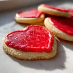 Close-up of heart-shaped sugar cookies topped with vibrant red sugar cookie icing recipe.