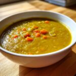 Close-up of a white bowl filled with thick, savory pea soup, topped with diced orange carrots.