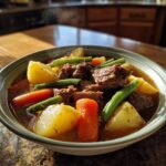 Close-up of a steaming bowl of vegetable beef soup filled with tender beef chunks, potatoes, carrots, and green beans.
