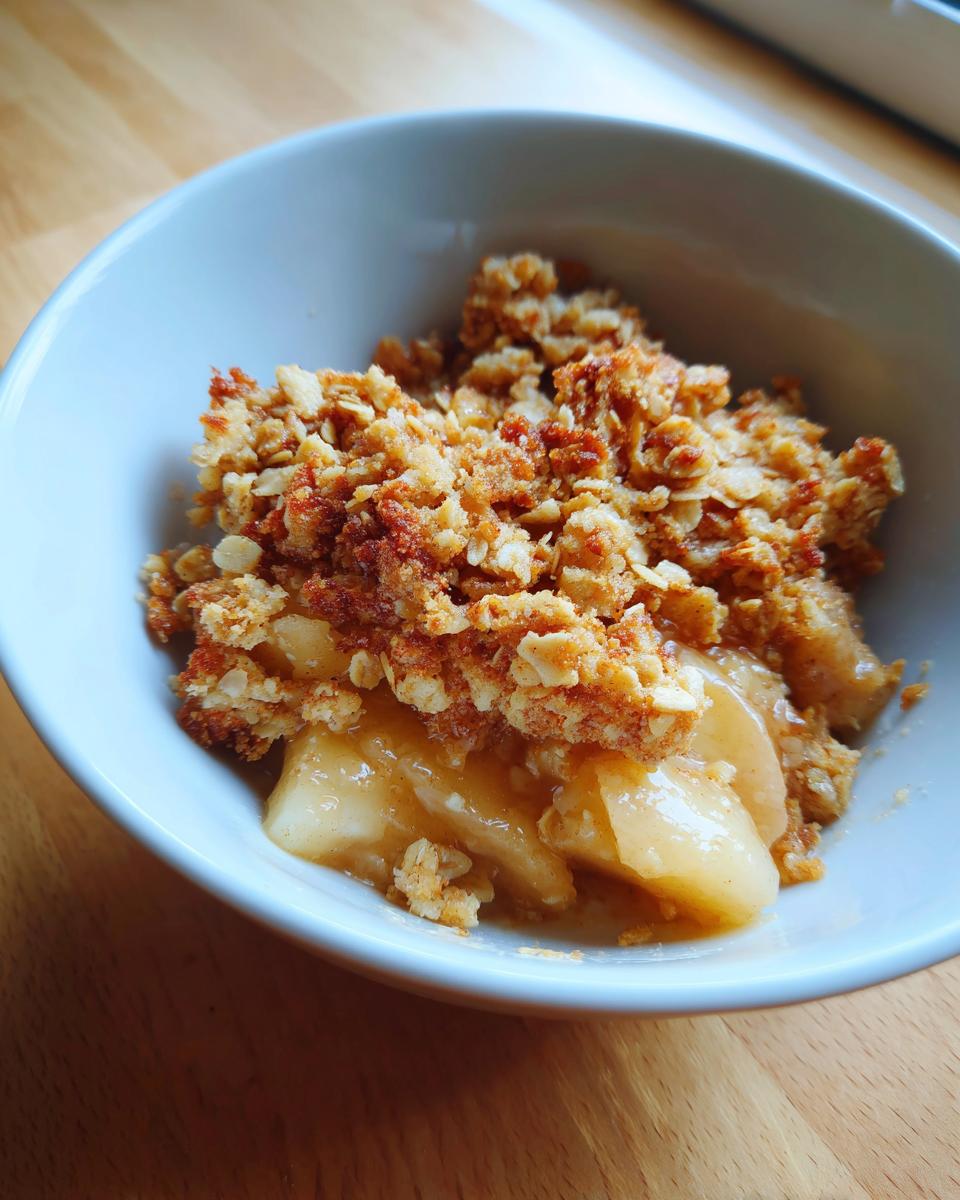 A close-up view of a serving of warm apple crumble with golden, crunchy topping and soft cooked apples underneath.