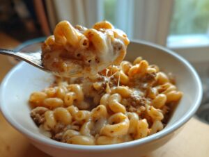 A spoonful of creamy homemade hamburger helper lifted from a white bowl, showing melted cheese strings.