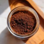 Overhead view of rich brown homemade hot cocoa mix powder stored in a clear glass jar.