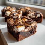 Close-up of a rich hot chocolate brownie square topped with toasted marshmallows and chocolate drizzle.