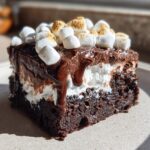 A decadent slice of hot chocolate poke cake topped with whipped cream, chocolate ganache, and toasted mini marshmallows.