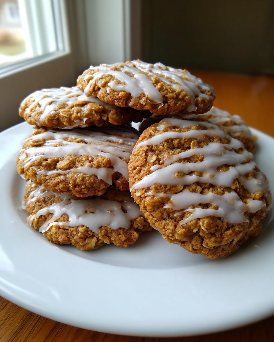 A stack of freshly baked iced oatmeal cookies drizzled with white vanilla glaze, sitting on a white plate.